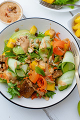 Healthy summer fresh salad with mango, avocado, lime and tofu with sweet peanut butter dressing on white wooden table