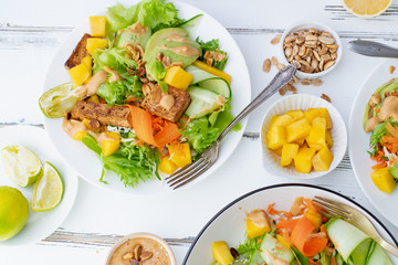 Healthy summer fresh salad with mango, avocado, lime and tofu with sweet peanut butter dressing on white wooden table