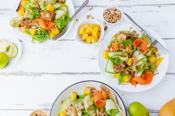 Healthy summer fresh salad with mango, avocado, lime and tofu with sweet peanut butter dressing on white wooden table