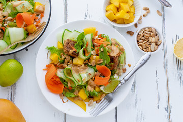 Healthy summer fresh salad with mango, avocado, lime and tofu with sweet peanut butter dressing on white wooden table