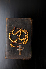 Rosary beads and prayer book on dark background.