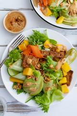 Healthy summer fresh salad with mango, avocado, lime and tofu with sweet peanut butter dressing on white wooden table