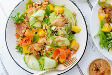 Healthy summer fresh salad with mango, avocado, lime and tofu with sweet peanut butter dressing on white wooden table