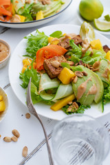 Healthy summer fresh salad with mango, avocado, lime and tofu with sweet peanut butter dressing on white wooden table