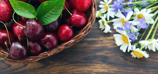 Cherries in the basket pot and daisies on an old wooden background.