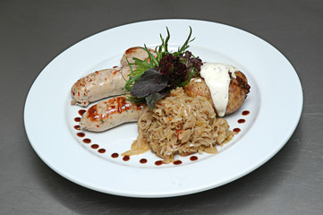 Grilled sausages stuffed potatoes, white sauce and stewed cabbage on a plate. Isolated on gray background