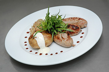 Grilled sausages stuffed potatoes, white sauce and stewed cabbage on a plate. Isolated on gray background