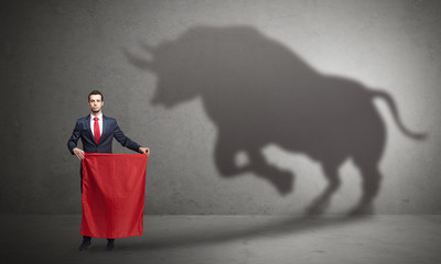 Businessman standing with red cloth in his hand and big bull shadow on the wall
