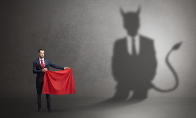 Businessman standing with red cloth in his hand and devil shadow on the background
