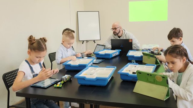 Group of teenage kids build their plastic toys under the guardian of their teacher at the engineering class slow motion