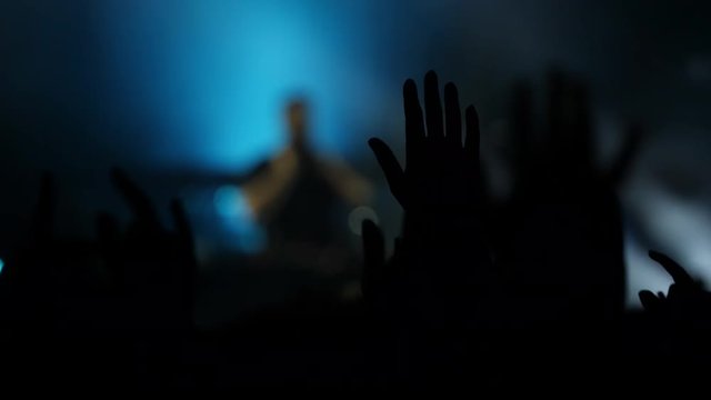 Silhouette of hands in the air at a live music concert with flashing strobe lighting