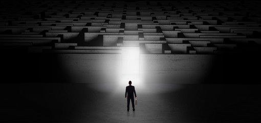 Businessman getting ready to enter the dark labyrinth with illuminated door
