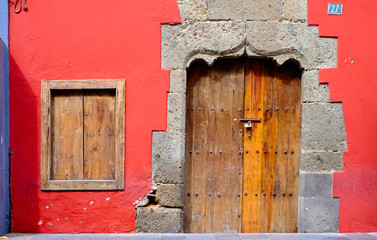Old house, a red wall, a boarded window and a closed timber door.