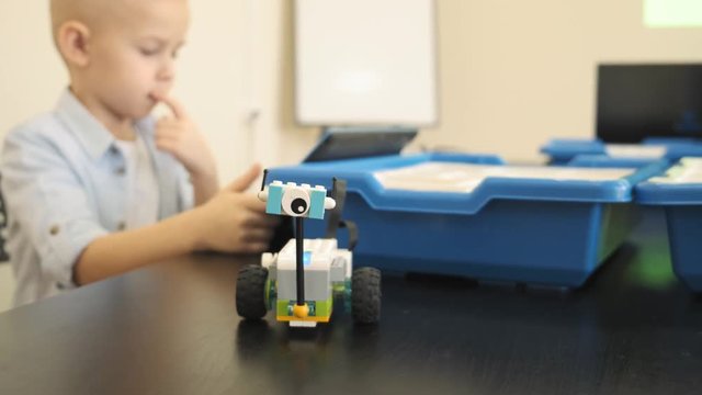 Close up view of nice electronic mini robot car standing on the table and the blond child on the backgroung slow motion