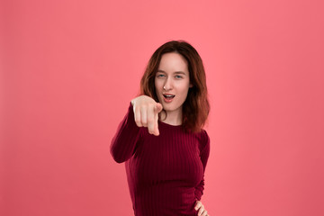 Happy young lady standing isolated over dark pink background looks at the camera while pointing at you