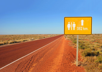 A graphics board on abandoned road in wasteland shows the distance and the direction of the way to the toilets.
