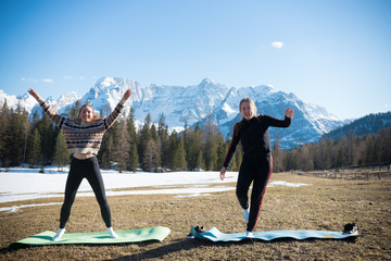 Dolomites - Two young funny women doing fitness on yoga mats on a background of the forest