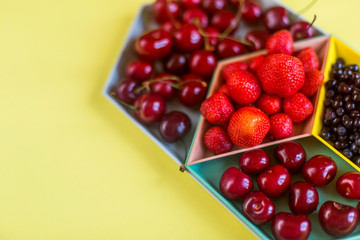 Cherries, strawberries, blue berries on yellow background. Colorful concept. Natural organic vegan healthy fresh food.