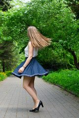 Young woman spinning in the park. The girl in the blue skirt is dancing on the street