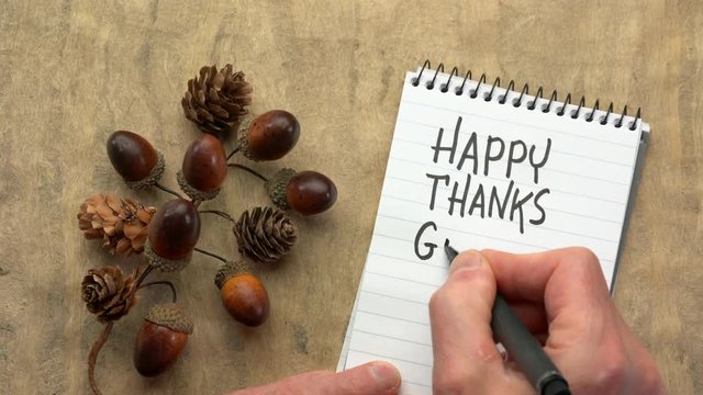 Happy Thanksgiving - man hand writing a note with a black marker in a spiral notebook, overhead view