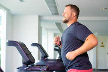 chubby man walking on running track, warming up on gym treadmill. - obrazy, fototapety, plakaty