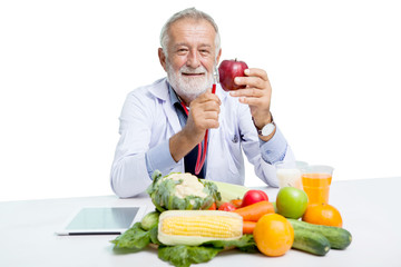 senior doctor male nutritionist holding stethoscope and red apple with Vegetables,Juice,fruit,milk while sitting at table on white background, elderly man dietitian with clipping path