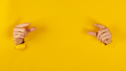 girl hand breaks the yellow paper and shows a gesture with two hands