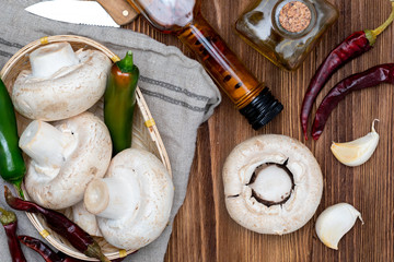 Basket of mushrooms (champignon, cut feet, Agaricus Bisporus) raw (uncooked). With several ingredients (olive oil, garlic and chilli pepper). Wood background and home appearance.