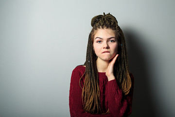 Close up shot of flirty emotional young pretty caucasian teenage girl with african braids and in maroon sweater. Teenager bites her lips. Card of emotions.