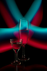 A two wine glass isolated on a black background with red white pink and orange neon light painting streaks of light behind them