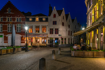 Fototapeta na wymiar Old street with tables of cafe in Bruges (Brugge), Belgium. Night cityscape of Bruges. Typical architecture of Bruges
