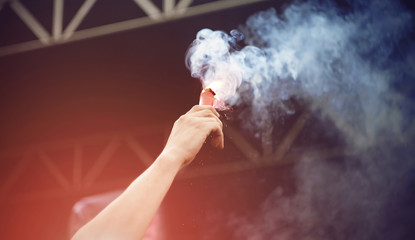 The man holds in his hand a beautiful red signal light emitting blue smoke that develops in the wind.