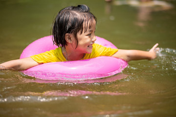 Little girl in pink pool ring swimming in water