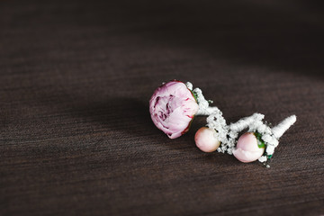 The bride holding in hand close-up the groom's buttonhole flowers with white roses, and green and greenery. Bride's Preparations. Wedding concept.