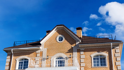 The roof windows and balcony of the house is pastel yellow and brown against a blue sky with light clouds. Bright sunny daylight. Place for text, minimalism. The concept of building houses, cottages.