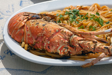 Delicious lunch by the sea. A white plate of spaghetti with huge lobsters on the grill. Travel to Santorini, Greece. Old port of Fira.