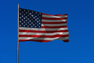 Flag of USA waving in the wind on flagpole against the sky with clouds on sunny day, banner, close-up