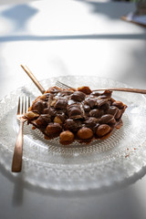 Bubble waffle with chocolate on a transparent plate with an antique design with golden fork and knife on white wooden table
