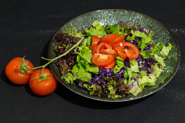 salad with tomatoes,lettuce,red cabbage and olive oil in the plate on the black background.