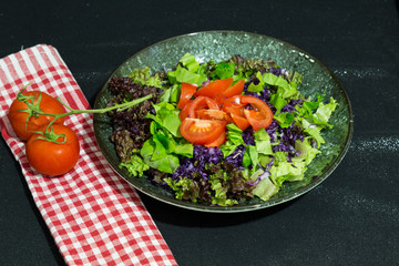 salad with tomatoes,lettuce,red cabbage and olive oil in the plate on the black background.