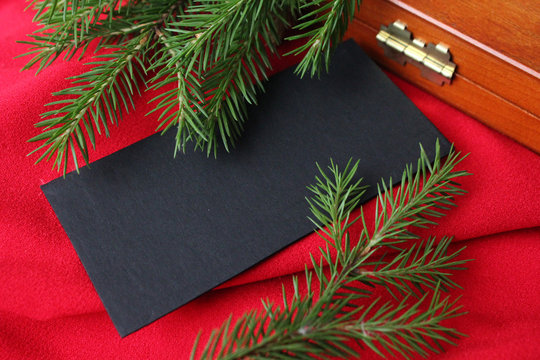 Christmas card background. New year holiday. Christmas still life. The view from the top. Free space for text. Green pine branches on a red background. Creative composition with a black card for greet