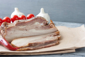 Baked slice of pork peritoneum with layers of fat with vegetables on a wooden table.
