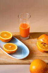 Female hand squeezes fresh cold orange into the glass. Sliced citrus on a wooden board and a blue plate. Orange juice for breakfast, vitamins for health.
