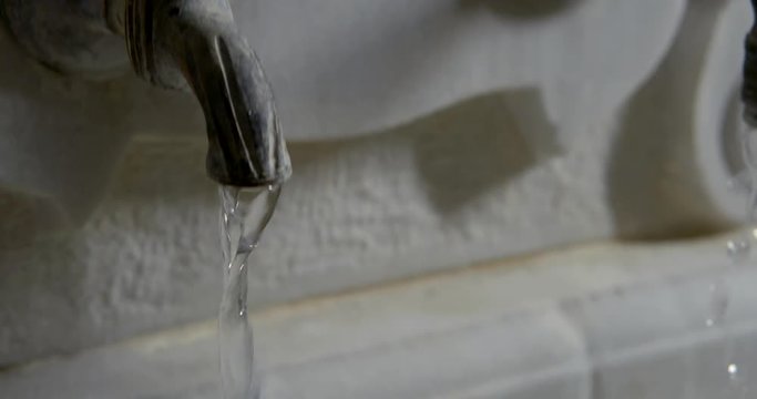clear water is pouring from two old stone tap of beautiful fountain, close-up