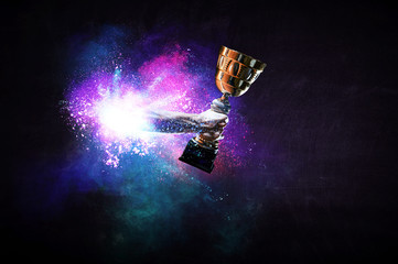 Hands holding champion cup on colourful splashes background. Mixed media