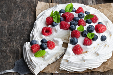 Pavlova meringue nest with berries and mint leaves on wooden table