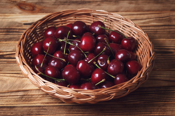 Dark red sweet cherry in wicker plate in rustic style on wooden table closeup