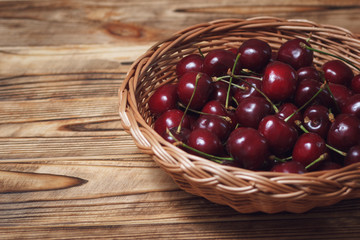 Wooden table with wicker plate full of dark red cherry, with copyspace area for captions