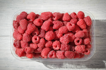 Red raspberry in container on white wooden table, top view