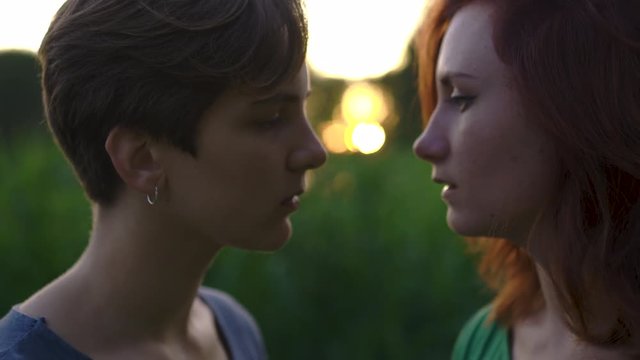 Two serious women with closed eyes enjoying sunset in front of high grass almost kissing with lips close to each other